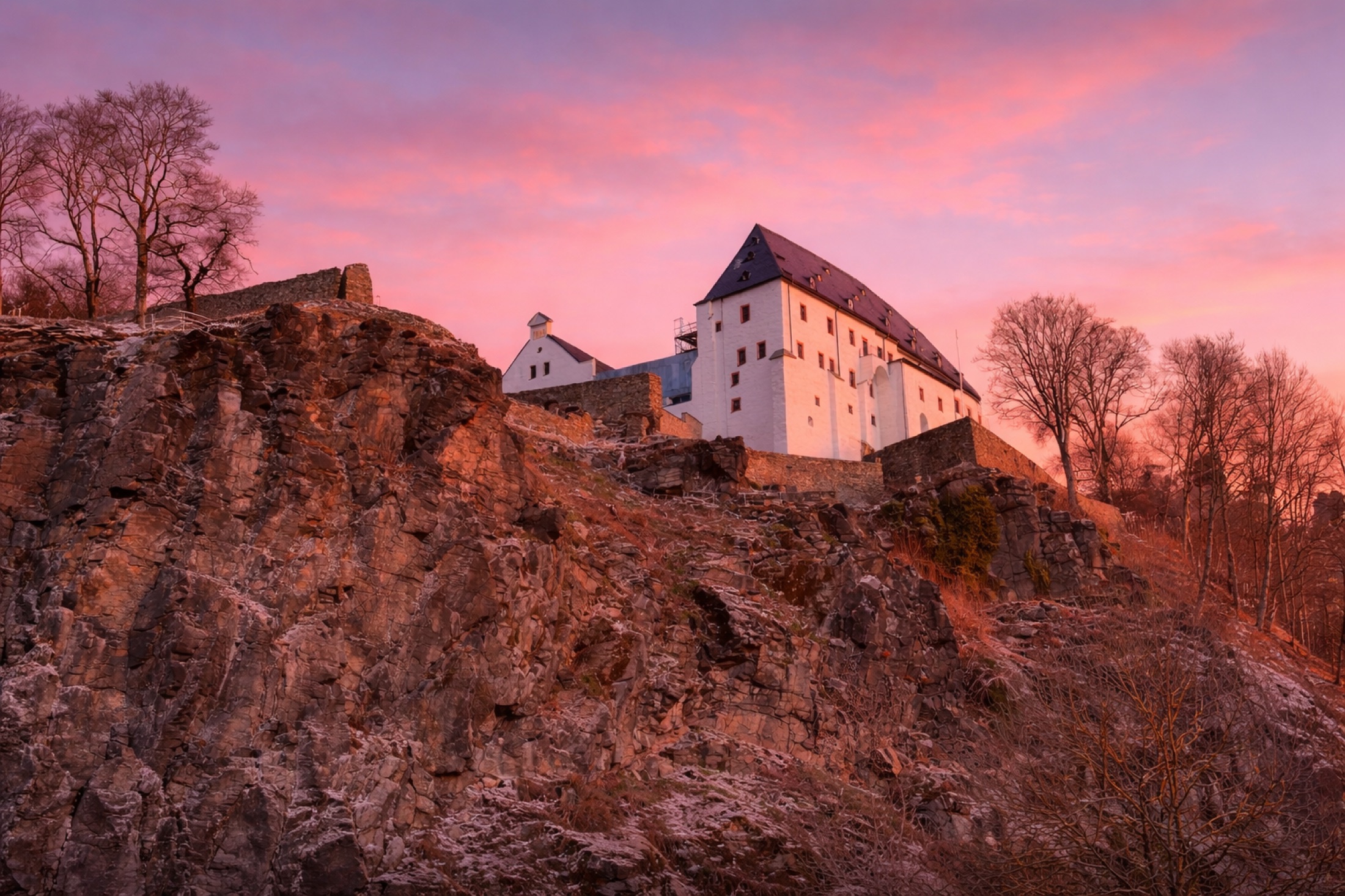 Historische Burg auf einem Felsen unter rosafarbenem Abendhimmel